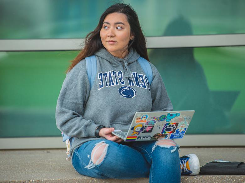 Student wearing Penn State gear works on laptop outside Gaige building