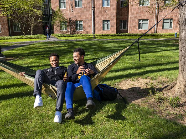 Two students sit on a hammock near residence halls.